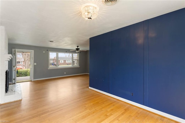 interior space with a ceiling fan, wood finished floors, visible vents, baseboards, and a brick fireplace