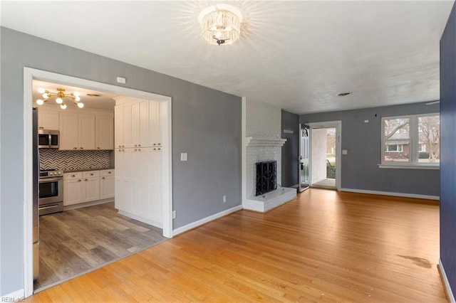 unfurnished living room with baseboards, light wood-style floors, an inviting chandelier, and a fireplace