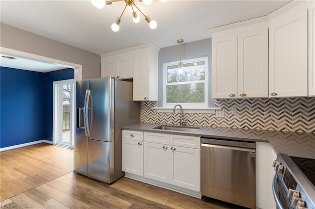 kitchen with a sink, white cabinetry, stainless steel appliances, light wood finished floors, and decorative backsplash