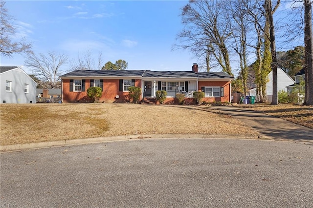 ranch-style house with a front lawn, brick siding, covered porch, and a chimney