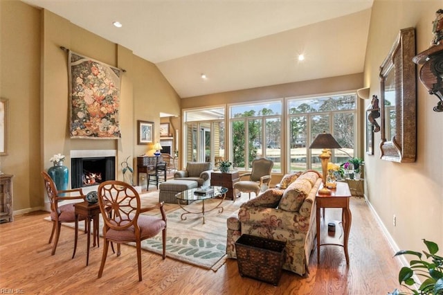 living room with high vaulted ceiling, a warm lit fireplace, wood finished floors, recessed lighting, and baseboards