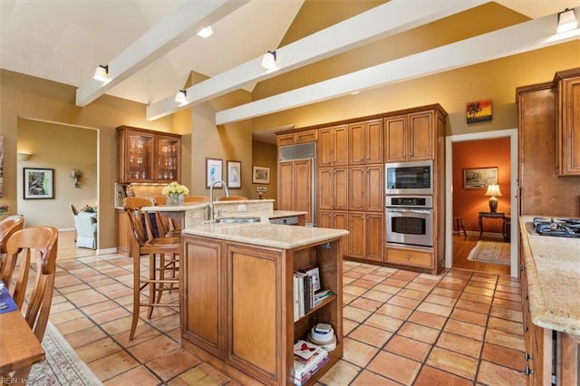 kitchen featuring built in appliances, light tile patterned floors, a kitchen breakfast bar, brown cabinetry, and a sink