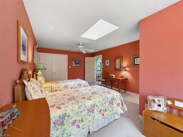 bedroom featuring baseboards, ceiling fan, carpet flooring, a skylight, and a closet