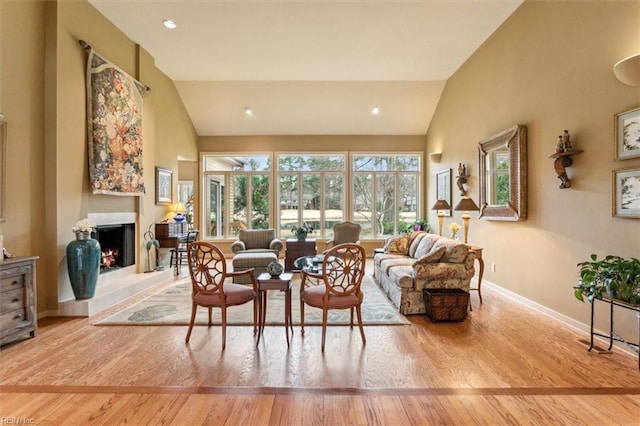 dining room featuring baseboards, a lit fireplace, recessed lighting, wood finished floors, and high vaulted ceiling