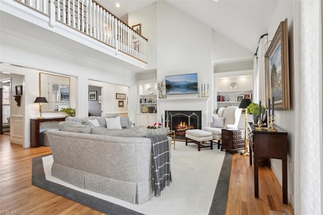 living room with built in features, a lit fireplace, and wood finished floors