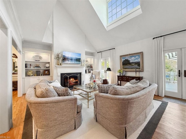 living area with built in features, high vaulted ceiling, a warm lit fireplace, and wood finished floors