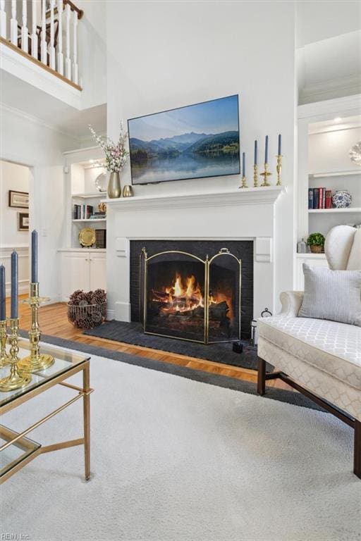 living area featuring built in features, a warm lit fireplace, wood finished floors, and crown molding