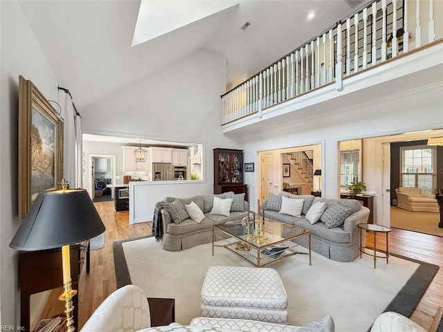 living room with a skylight, light wood-type flooring, and high vaulted ceiling