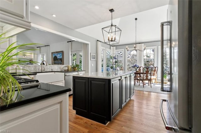 kitchen with light wood-type flooring, decorative light fixtures, dark cabinetry, stainless steel appliances, and a chandelier