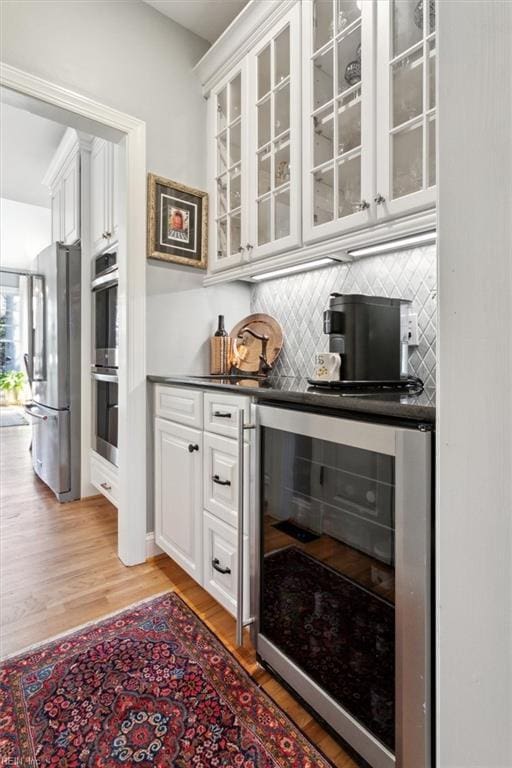 bar featuring beverage cooler, backsplash, appliances with stainless steel finishes, and light wood-style flooring