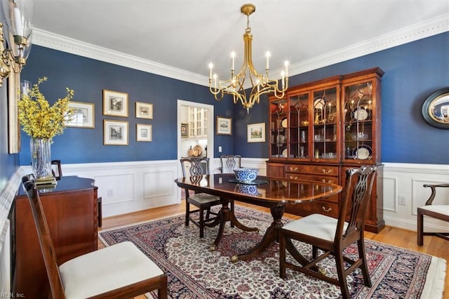 dining room with a wainscoted wall, a notable chandelier, wood finished floors, and ornamental molding