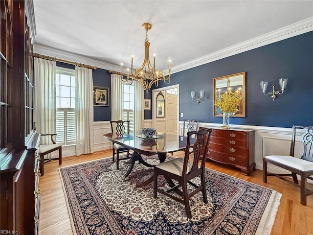 dining area with crown molding, light wood-type flooring, a wainscoted wall, and a chandelier