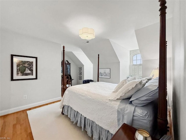 bedroom featuring visible vents, baseboards, light wood-style floors, and vaulted ceiling