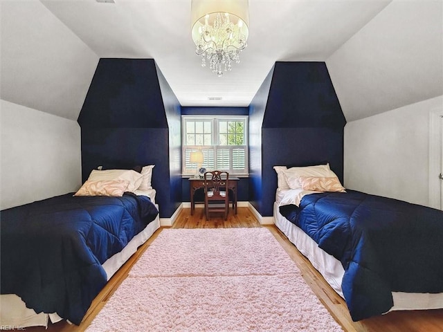 bedroom featuring an inviting chandelier, wood finished floors, baseboards, and lofted ceiling