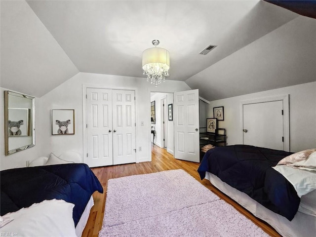 bedroom featuring lofted ceiling, a notable chandelier, light wood-style floors, and a closet