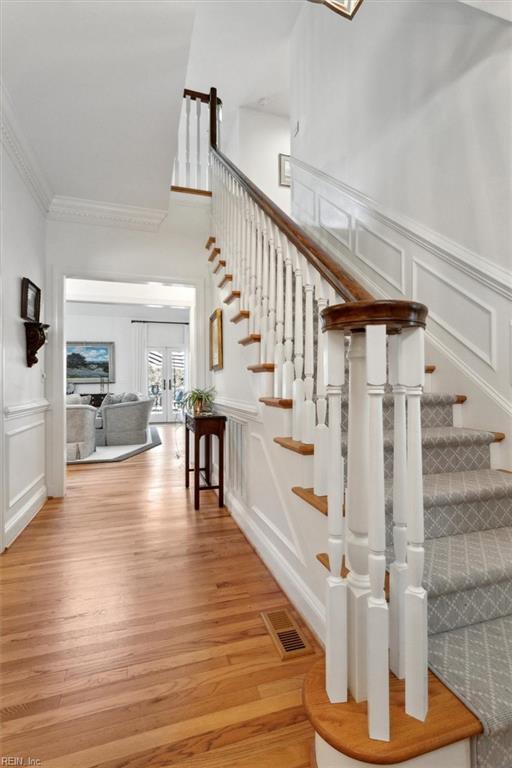 staircase featuring wood finished floors, visible vents, wainscoting, crown molding, and a decorative wall