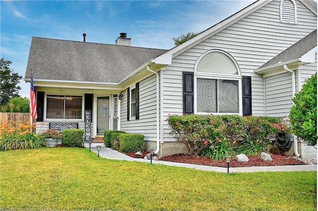 view of front of home featuring roof with shingles, a chimney, a front lawn, and fence