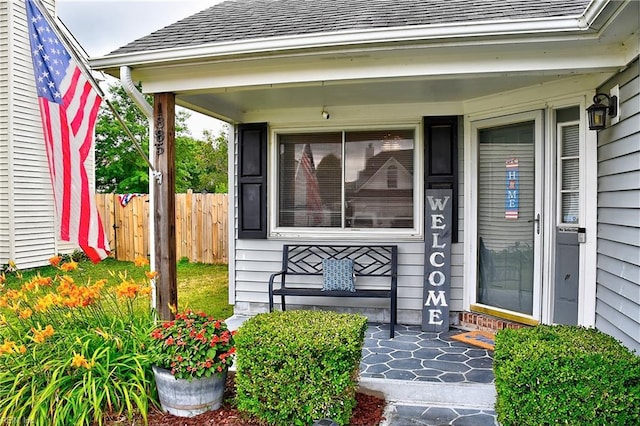 doorway to property featuring a porch, a shingled roof, and fence