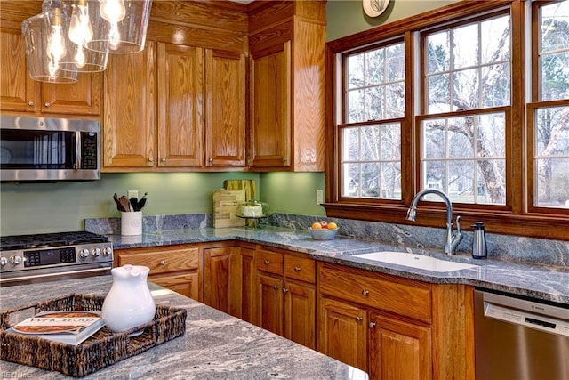 kitchen featuring brown cabinets, pendant lighting, a sink, dark stone countertops, and stainless steel appliances