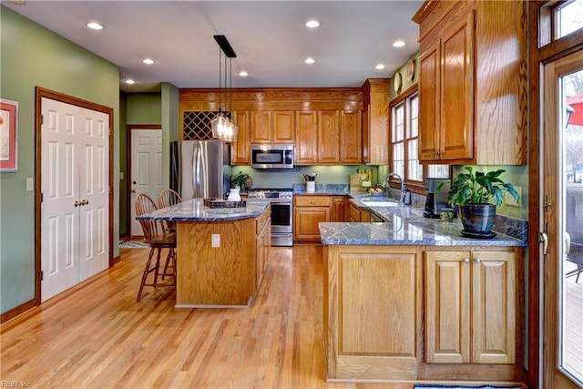 kitchen with brown cabinetry, light wood finished floors, a sink, stainless steel appliances, and a kitchen breakfast bar