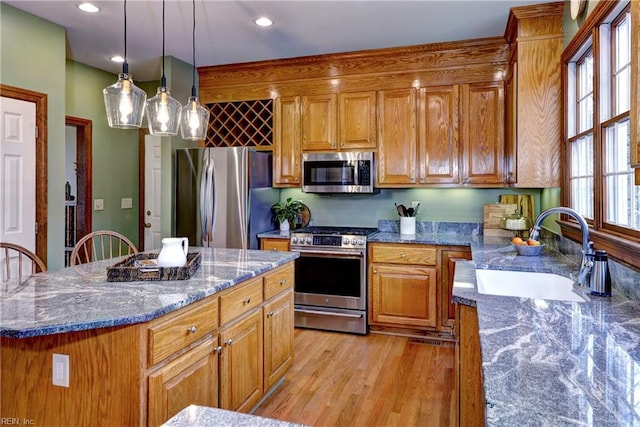 kitchen with a sink, a kitchen island, stainless steel appliances, light wood-style floors, and brown cabinetry