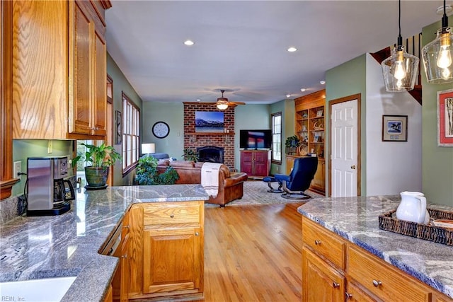 kitchen with light wood-style floors, a peninsula, brown cabinetry, a brick fireplace, and ceiling fan