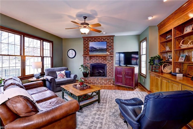 living area featuring a brick fireplace, wood finished floors, baseboards, and ceiling fan