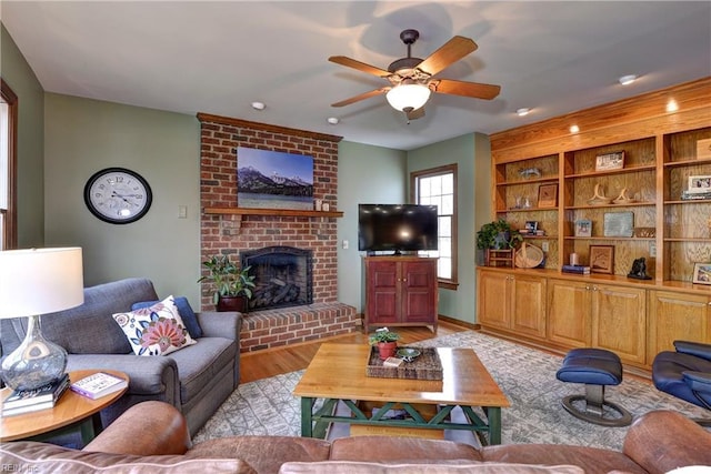 living room with light wood-style floors, a brick fireplace, and ceiling fan