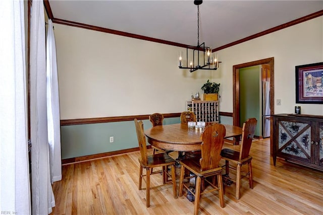 dining space with an inviting chandelier, crown molding, light wood-style floors, and baseboards