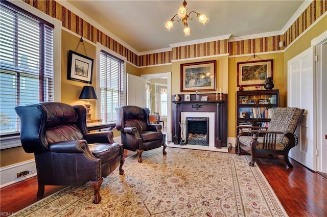 sitting room with a notable chandelier, ornamental molding, wood finished floors, a fireplace, and baseboards