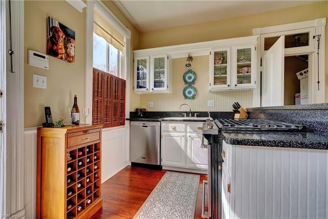 kitchen with dark wood-type flooring, a sink, white cabinetry, appliances with stainless steel finishes, and wainscoting