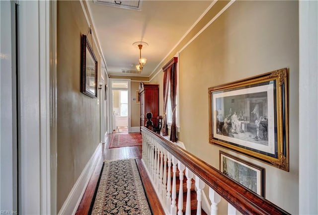 hall with crown molding, wood finished floors, visible vents, and baseboards