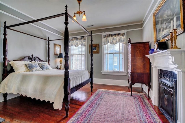 bedroom featuring visible vents, wood finished floors, a fireplace, crown molding, and baseboards