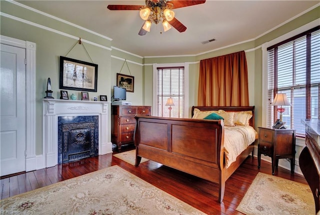 bedroom with a high end fireplace, visible vents, crown molding, ceiling fan, and dark wood-type flooring