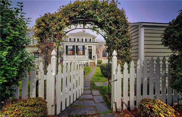 gate at dusk with covered porch and a fenced front yard