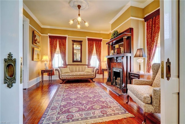 living room with hardwood / wood-style floors, baseboards, a fireplace with raised hearth, crown molding, and a chandelier