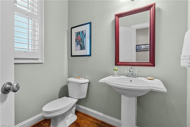 half bath with baseboards, toilet, and wood finished floors