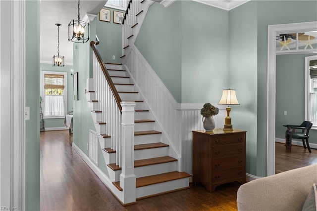 staircase with a chandelier, ornamental molding, baseboards, and wood finished floors