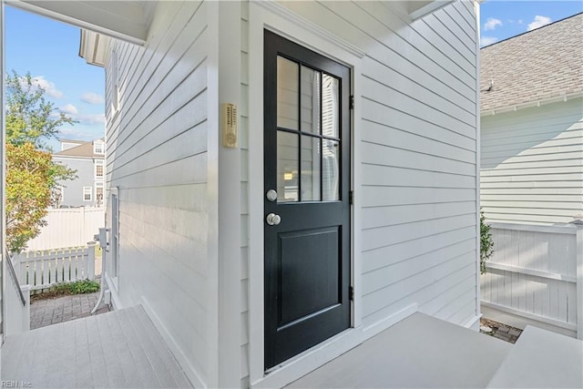 view of exterior entry with fence and roof with shingles