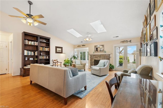 living area with vaulted ceiling with skylight, light wood-style flooring, plenty of natural light, and ceiling fan