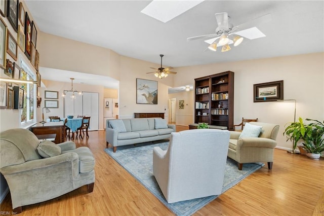 living area with light wood-type flooring, vaulted ceiling with skylight, baseboards, and ceiling fan with notable chandelier