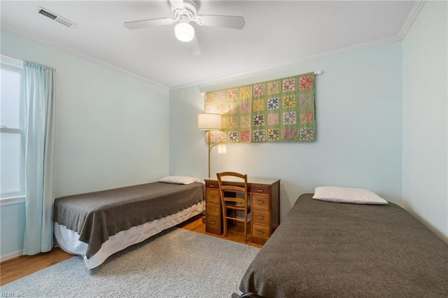 bedroom with visible vents, ornamental molding, ceiling fan, and wood finished floors