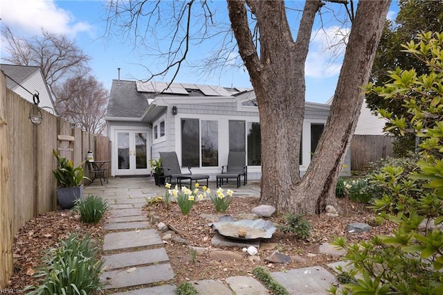 rear view of property with french doors, roof mounted solar panels, a fenced backyard, and a patio area