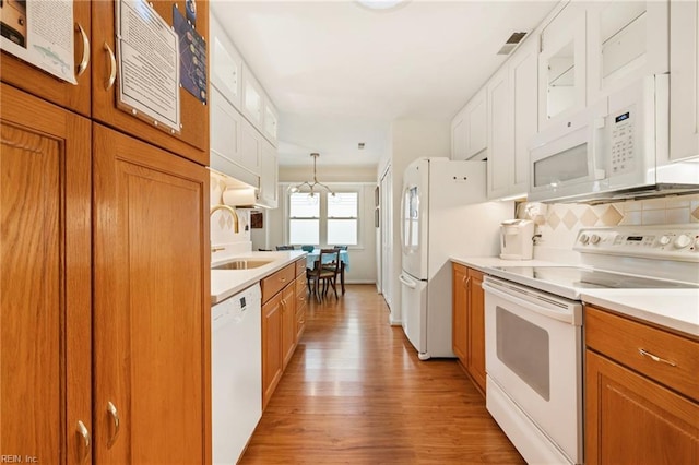 kitchen featuring tasteful backsplash, glass insert cabinets, light wood-style floors, white appliances, and a sink