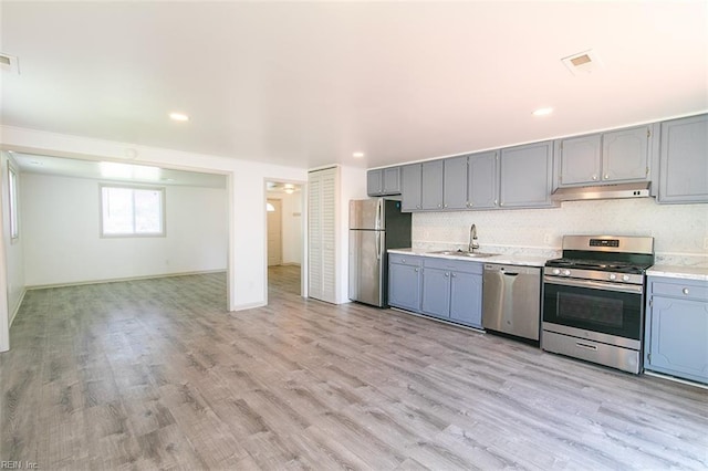 kitchen with gray cabinets, a sink, light countertops, under cabinet range hood, and appliances with stainless steel finishes