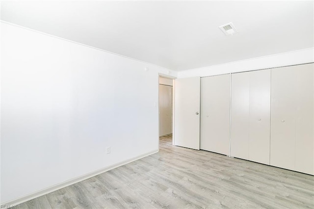 unfurnished bedroom featuring a closet, visible vents, baseboards, and wood finished floors