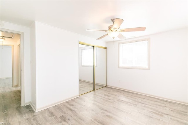 unfurnished bedroom featuring a ceiling fan, attic access, light wood-style floors, a closet, and crown molding