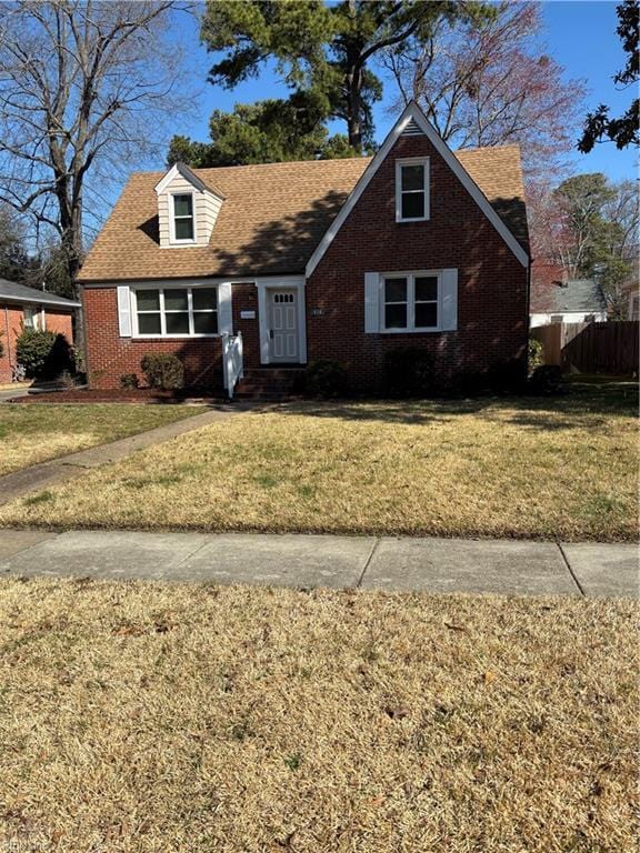 view of front facade featuring brick siding, roof with shingles, a front yard, and fence