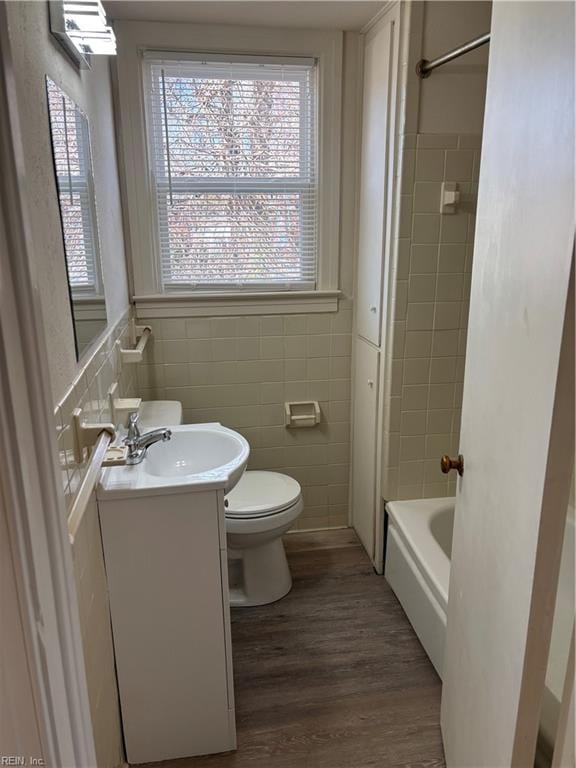 bathroom with vanity, wood finished floors, bathing tub / shower combination, tile walls, and toilet