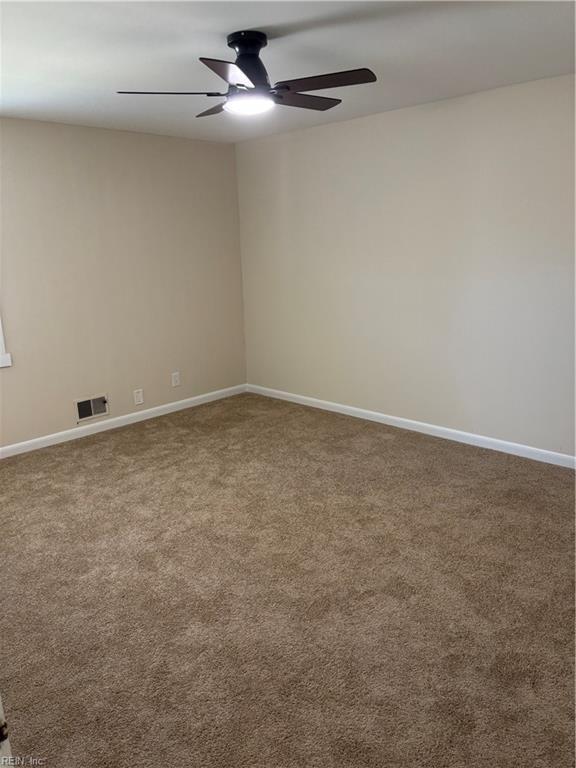 carpeted empty room with visible vents, a ceiling fan, and baseboards